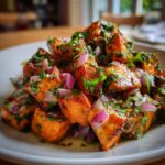 Close-up of a bright orange sweet potato salad featuring roasted chunks, red onion, and a vibrant green herb dressing.