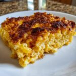 A close-up of a square serving of baked mac and cheese recipe with a deeply browned, crispy topping.