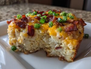 A close-up of a serving of baked potato casserole topped with melted cheddar, bacon bits, and green onions.