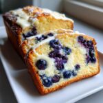 Close-up of sliced Blueberry Cream Cheese Bread showing moist crumb, blueberries, and cream cheese swirls, topped with a light glaze.