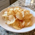A white bowl filled with freshly made, lightly seasoned air fryer potato chips resting on a granite countertop.