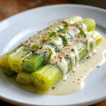 Close-up of tender braised leeks topped with a creamy white sauce and cracked black pepper.