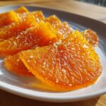 Close-up, sunlit photo of glistening candied orange slices arranged on a white plate.