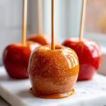 Close-up of a glossy, homemade caramel apple sprinkled with salt, ready to eat.