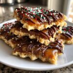 A stack of caramel ritz cracker christmas cookies topped with caramel, chocolate drizzle, and festive sprinkles.