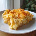 A close-up serving of creamy cheesy potato casserole topped with golden, crunchy cornflakes.
