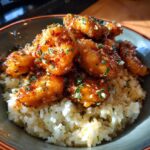 Close-up of glazed chicken scampi pieces served over a bed of garlic parmesan rice in a bowl.