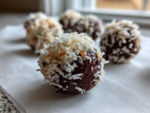 A close-up of a chocolate-dipped coconut ball generously coated in shredded coconut flakes.