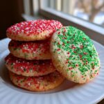 A stack of freshly baked christmas sprinkle sugar cookies topped with red, green, and white nonpareils.