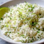 Close-up of fluffy cilantro lime rice topped with fresh cilantro and bright green lime zest, served with a lime wedge.