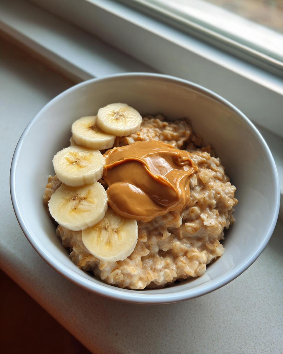 A bowl of creamy banana oatmeal topped with sliced bananas and a dollop of peanut butter.