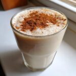 A glass filled with creamy coquito recipe, topped with a generous dusting of ground cinnamon.
