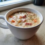 Close-up of a creamy white bean soup with chunks of ham and carrots, seasoned with herbs.