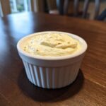 A small white ramekin filled with creamy horseradish sauce for prime rib, sitting on a dark wooden table.