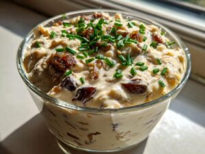 Close-up of creamy onion dip topped with caramelized onions and fresh chives in a glass bowl.