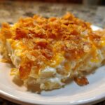A close-up of a creamy slice of potato casserole topped with melted cheese and crunchy cornflakes.