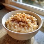 A close-up of creamy rice pudding recipe served in a white bowl, dusted generously with cinnamon.
