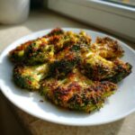 Close-up of crispy, baked smashed broccoli florets with a golden-brown crust on a white plate.