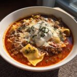 A hearty bowl of crockpot lasagna soup featuring rich broth, meat sauce, pasta pieces, melted cheese, and a dollop of ricotta.