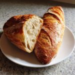 A golden-brown crusty french bread loaf, cut in half to show the airy interior crumb structure.