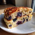 Close-up of fluffy sheet pan pancakes cut in half, showing juicy blueberries inside.