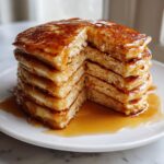 A tall stack of fluffy discard pancakes drizzled generously with golden maple syrup.