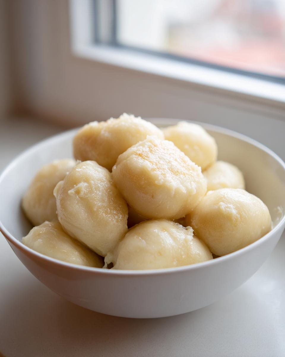 A white bowl filled with freshly made, fluffy potato dumplings, lightly glistening.