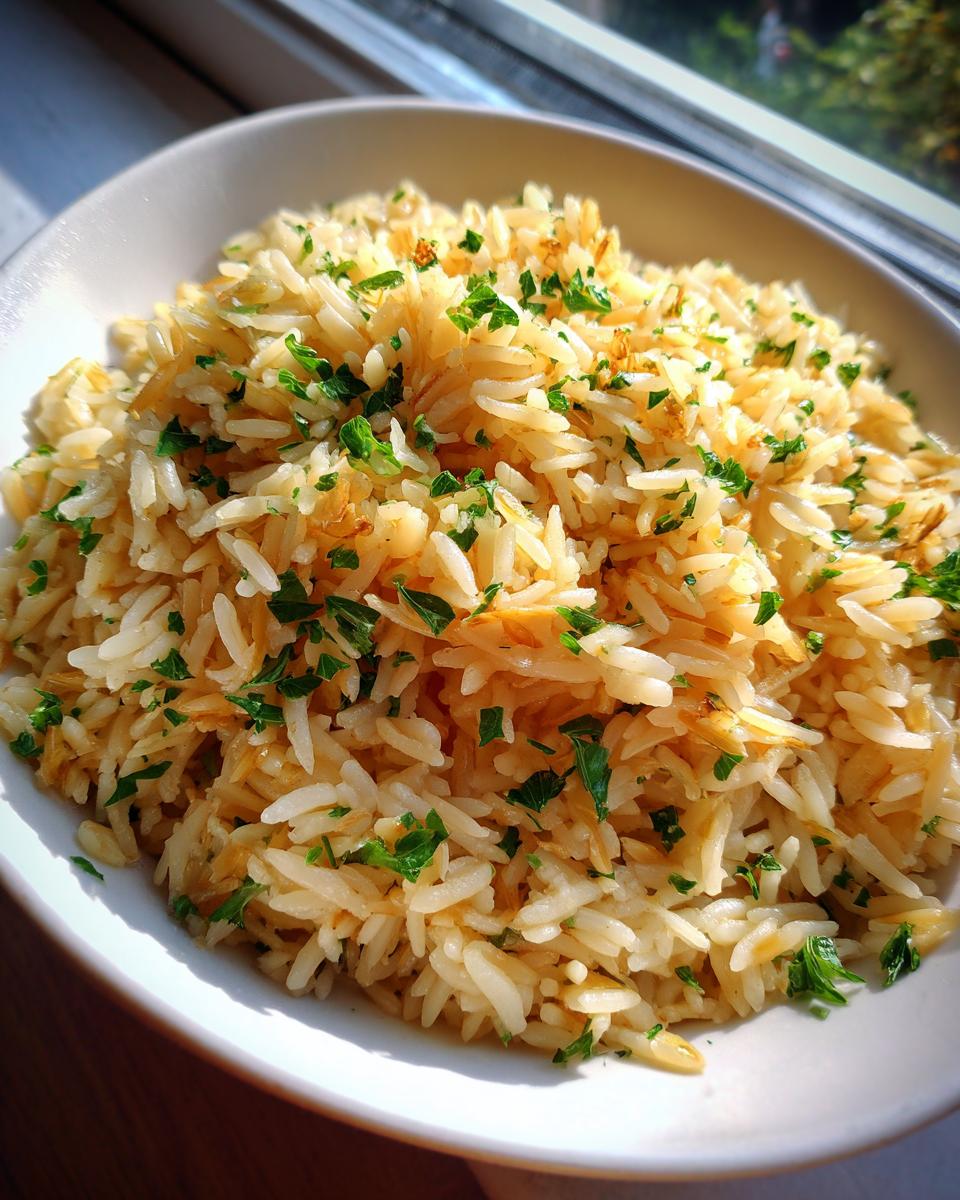 A close-up of fluffy rice pilaf mixed with toasted vermicelli and topped with fresh chopped parsley.