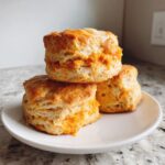 Three fluffy sweet potato biscuits stacked on a white plate, with butter melting on top of the uppermost biscuit.