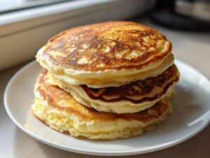 A tall stack of golden brown, fluffy pancakes sitting on a white plate.