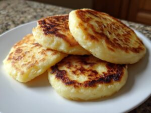 Four golden-brown, pan-fried irish potato farls stacked slightly on a white plate.