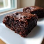 Close-up of a fudgy square of date brownies topped with chocolate chips on a white plate.