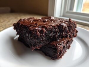 Two stacked, rich, fudgy date brownies with a shiny top, served on a white plate.