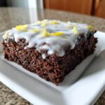 A close-up of a fudgy, dark chocolate lemon brownies square topped with white glaze and lemon zest.