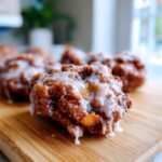 Close-up of a freshly glazed, golden-brown apple fritter sitting on a wooden cutting board.
