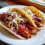 Close-up of two soft tortilla salmon tacos filled with glazed salmon pieces and colorful coleslaw.