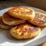 A stack of four golden-brown, pan-fried irish potato farls resting on a white plate.