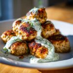 A stack of golden brown greek chicken meatballs generously drizzled with creamy tzatziki sauce and fresh dill.