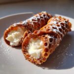 Close-up of two freshly made cannoli filled with sweet ricotta cream and dusted with powdered sugar.