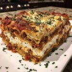 A thick, layered slice of homemade lasagna showing meat sauce, ricotta cheese, and pasta, topped with melted cheese and parsley.