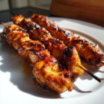 Three perfectly grilled honey garlic chicken skewers resting on a white plate, showing caramelized glaze.