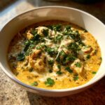 A close-up of a white bowl filled with creamy keto white chicken chili, topped with shredded cheese and fresh cilantro.