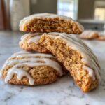 A stack of soft maple brown sugar cookies drizzled with white glaze, one cookie is broken open to show the chewy interior.