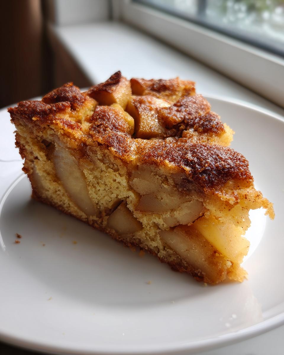 Close-up of a moist slice of jewish apple cake with visible chunks of baked apple and a caramelized cinnamon topping.