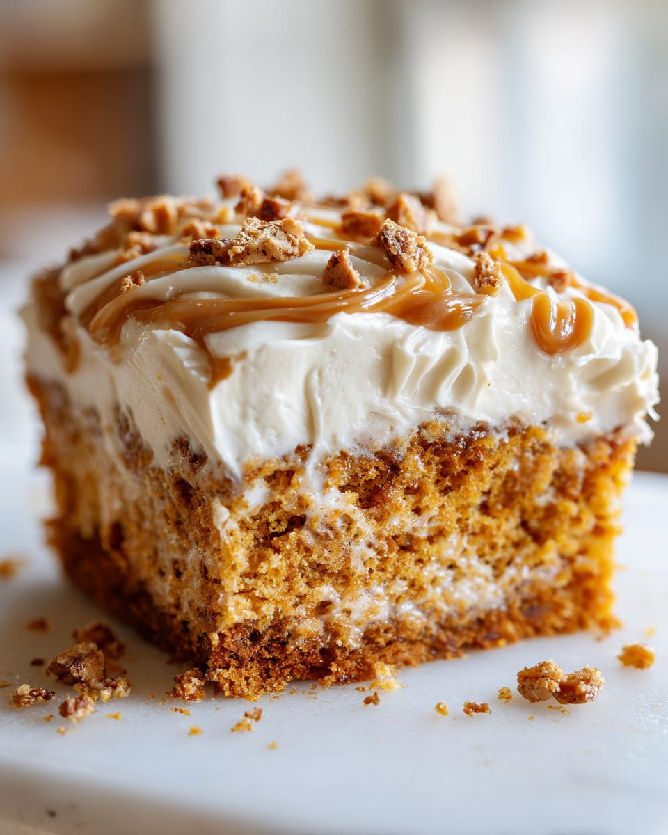 Close-up of a moist slice of pumpkin poke cake topped with cream cheese frosting, caramel drizzle, and pecans.