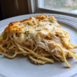 A close-up of a serving of Monterey chicken spaghetti with shredded chicken and a bubbly, cheesy topping.