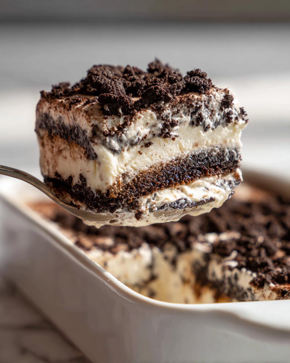 A spoonful of creamy, layered Oreo dirt cake being lifted from a white baking dish.