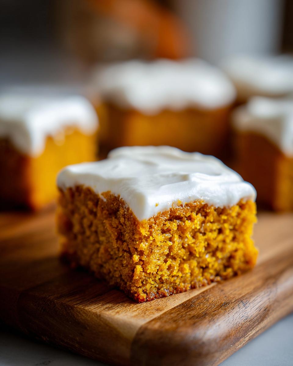 Close-up of a moist square of pumpkin bars with thick cream cheese frosting on a wooden board.