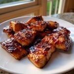 Close-up of glossy, caramelized salmon bites coated in homemade teriyaki sauce on a white plate.