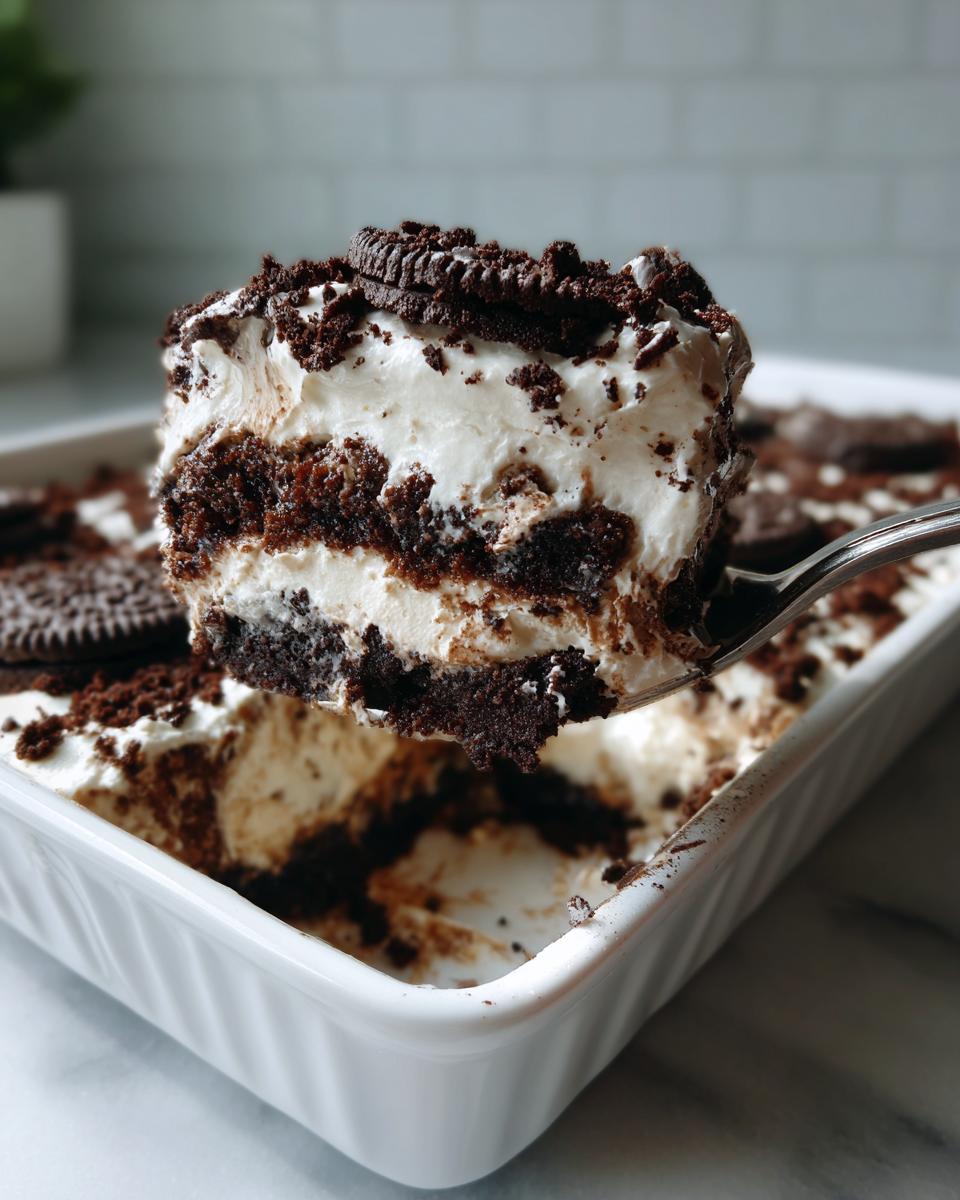 A spoonful of creamy, layered oreo dirt cake being lifted from a white dish.